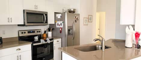 A modern kitchen with white cabinetry, a stainless steel refrigerator, a microwave, an oven, and a sink with a contemporary faucet.