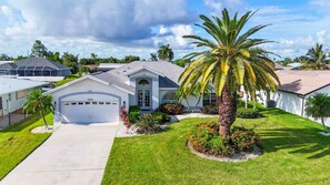 A residential house with a garage, a well-maintained lawn, and a palm tree. - Villa Dolphin – Prime Location, Southern Exposure, Pool & Gulf Access (Cape Coral)