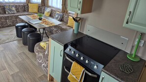 A compact kitchen with a stove, oven, and a dining area with a table and chairs. - 10 Berth Caravan Butlins Skegness Pet Friendly (Skegness)