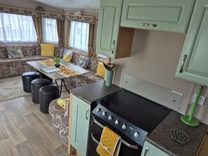 A compact kitchen with a stove, oven, and a dining area with a table and chairs. - 10 Berth Caravan Butlins Skegness Pet Friendly (Skegness)
