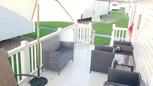 A covered outdoor deck with wicker furniture, a white railing, and a view of mobile homes in the background. - 10 Berth Caravan Butlins Skegness Pet Friendly (Skegness)