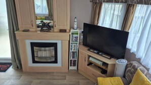 A living room with a fireplace, a flat-screen TV, a bookshelf, and a sofa. - 10 Berth Caravan Butlins Skegness Pet Friendly (Skegness)