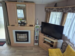 A living room with a fireplace, a flat-screen TV, a bookshelf, and a sofa. - 10 Berth Caravan Butlins Skegness Pet Friendly (Skegness)