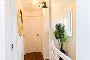 A hallway with a white door, a potted plant, and a light fixture. - House Sleeps 7 With Parking (Northampton)