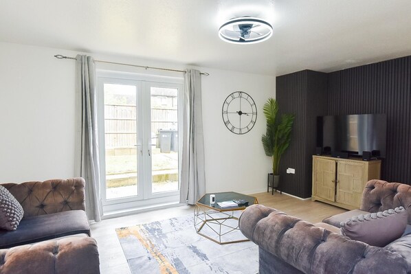 A living room with a sofa, a coffee table, a clock, a television, and a plant.