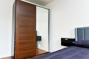 A bedroom with a wooden wardrobe, a bed with a blue headboard, and a small bedside table with a lamp. - House Sleeps 7 With Parking (Northampton)