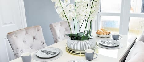 A dining table set with plates, cutlery, and a vase of white flowers.