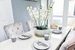 A dining table set with plates, cutlery, and a vase of white flowers. - House Sleeps 7 With Parking (Northampton)