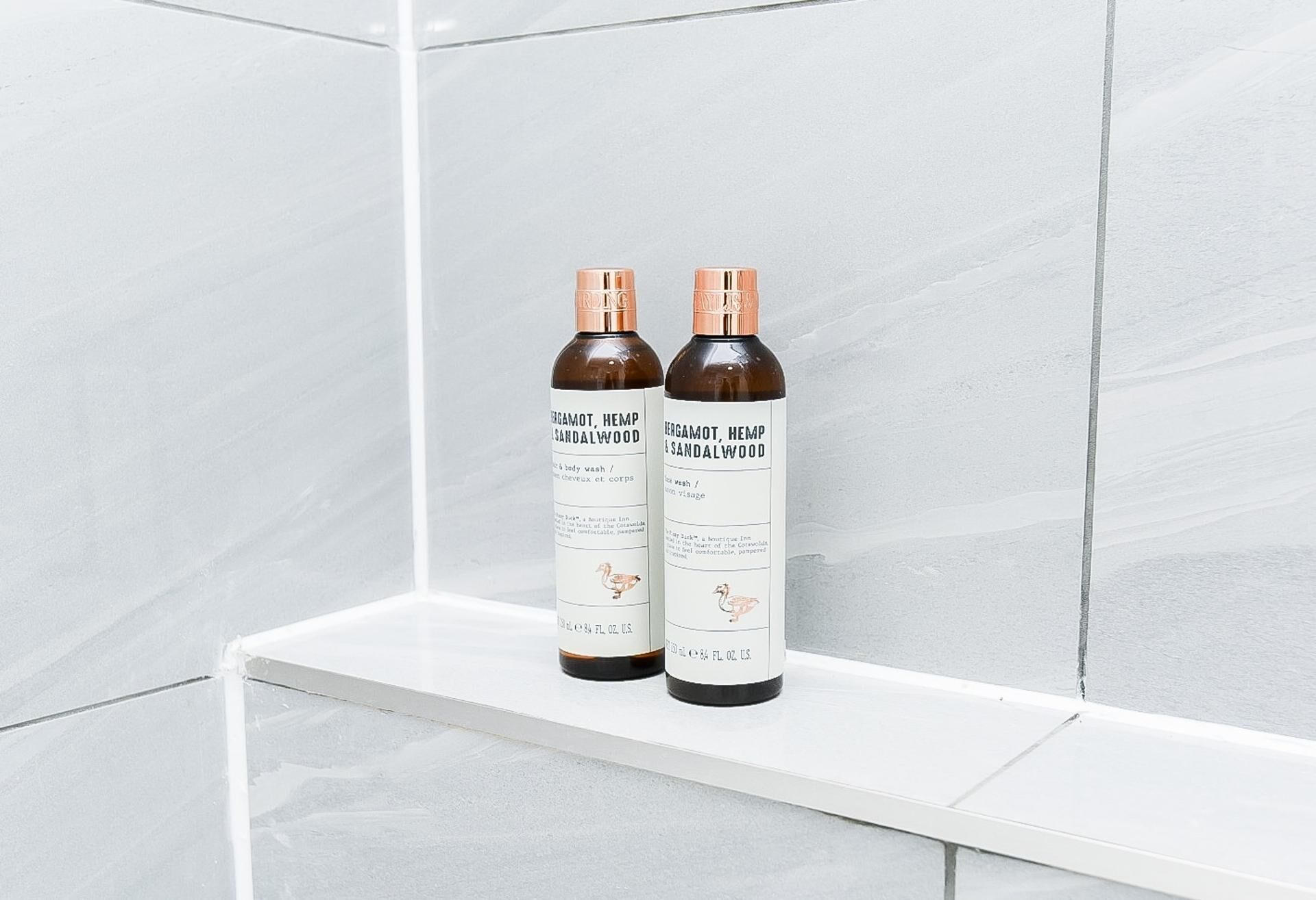 Two bottles of Bergamot, Hemp & Sandalwood on a white shelf in a bathroom with white tiles.