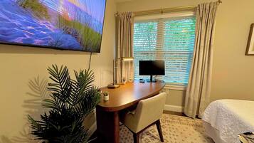 A hotel room with a desk, a computer, a TV, a bed, and a window with curtains.