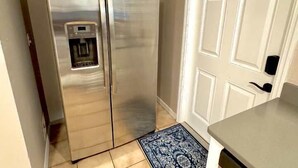 Un refrigerador de acero inoxidable con dispensador de agua, una puerta blanca con paneles y un tapete azul estampado.