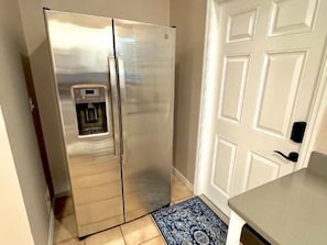 Ein Edelstahl-Kühlschrank mit Wasserspender, eine weiße Tür mit Füllungsmuster und ein blaues Teppichmuster.