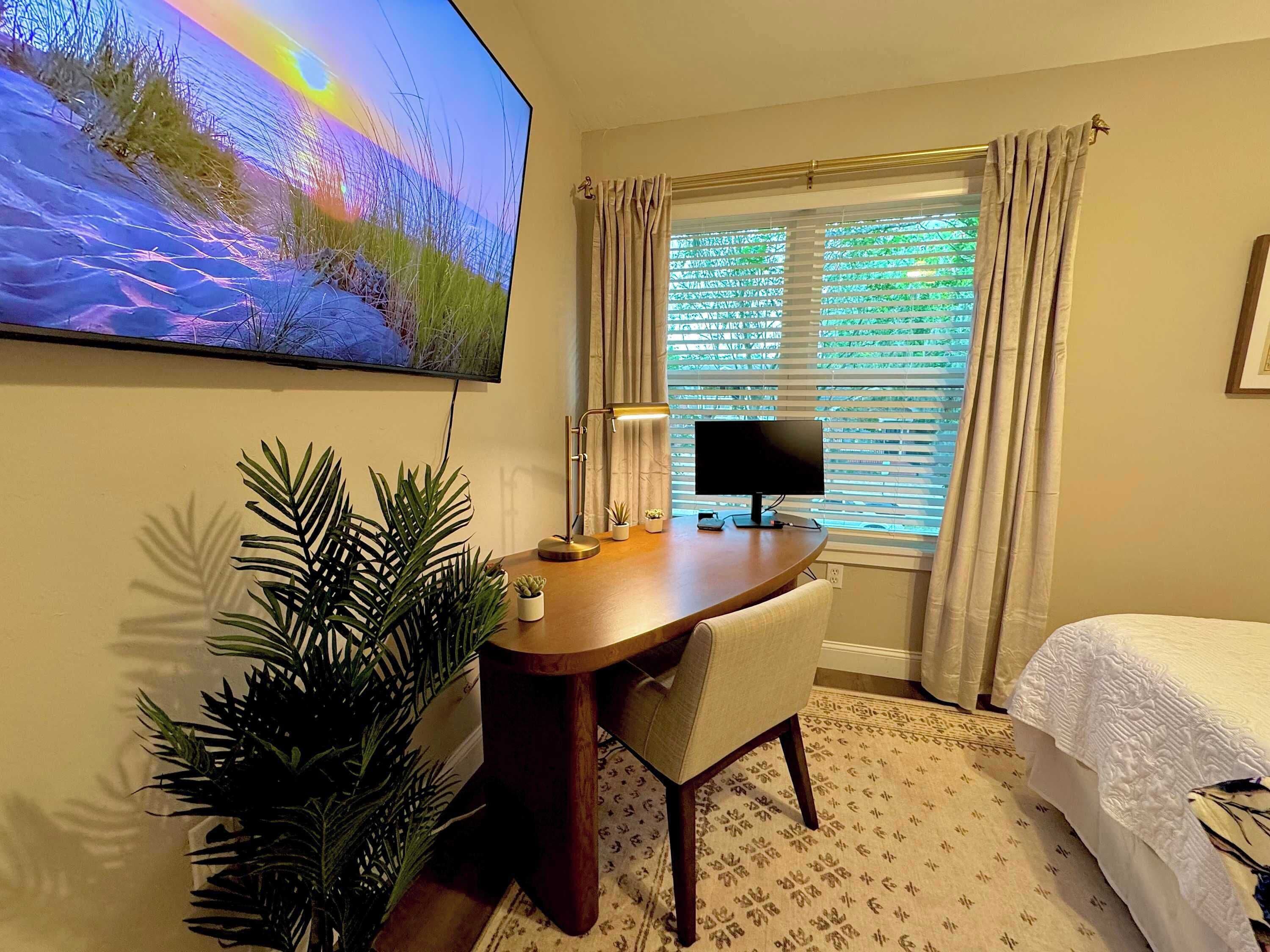 A hotel room with a desk, a computer, a TV, a bed, and a window with curtains.