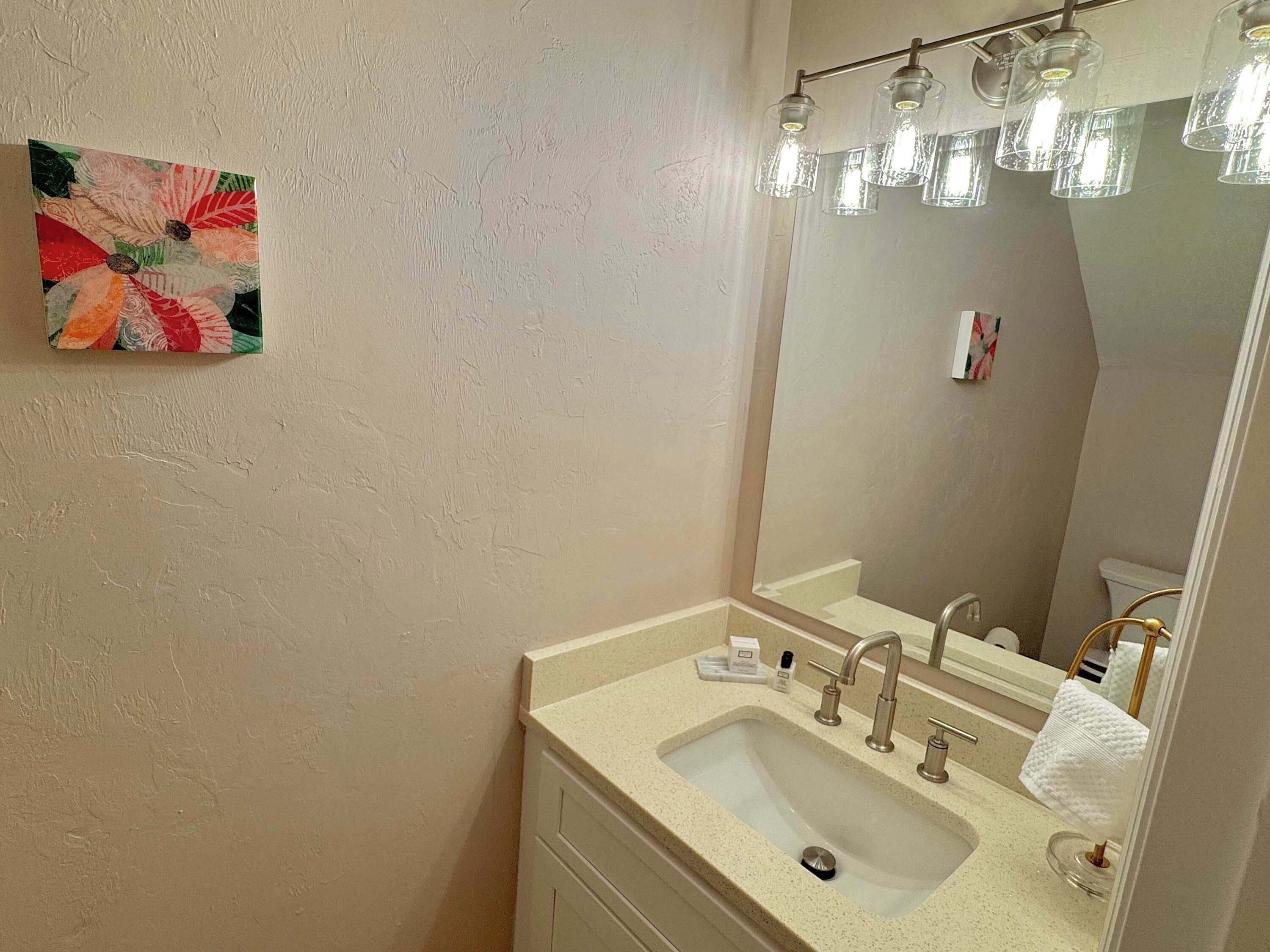 Un baño con lavamanos, espejo y una obra de arte floral en la pared.