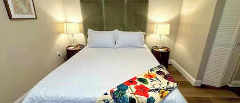 A neatly made bed with a floral throw, two bedside lamps, and a framed picture on the wall.