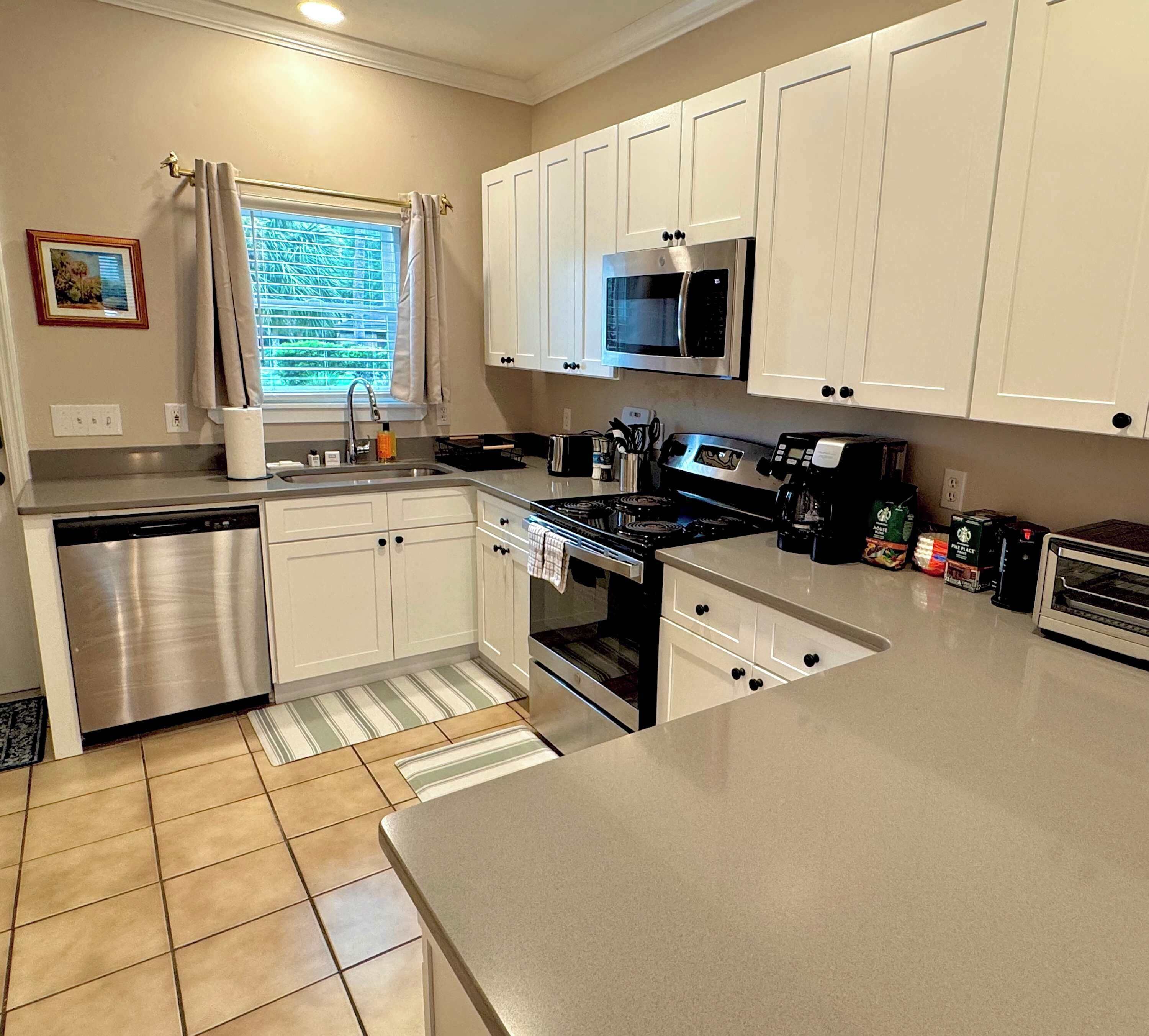 A kitchen with white cabinets, stainless steel appliances, and a window with curtains.