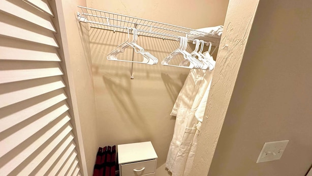 A narrow walk-in closet with a metal drying rack, a white cabinet with drawers, and a red plaid garment. - UF Campus Townhome - Full Kitchen 2 BR Pets OK (Gainesville)