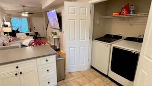 A compact kitchen with a built-in washer and dryer, a dining area with a table and chairs, and a television mounted on the wall. - UF Campus Townhome - Full Kitchen 2 BR Pets OK (Gainesville)