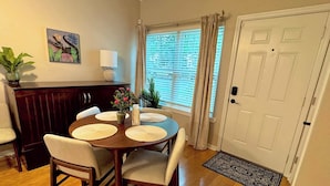 A dining area with a wooden table, four chairs, a vase with flowers, a lamp, and a window with blinds. - UF Campus Townhome - Full Kitchen 2 BR Pets OK (Gainesville)