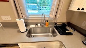 A modern kitchen with a stainless steel sink, a window with curtains, and a countertop with a dish rack and a bottle of soap. - UF Campus Townhome - Full Kitchen 2 BR Pets OK (Gainesville)