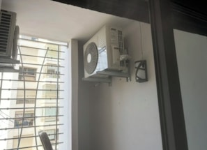 Eine Klimaanlage an der Wand, ein Fenster mit Gitterrost und ein Türrahmen.