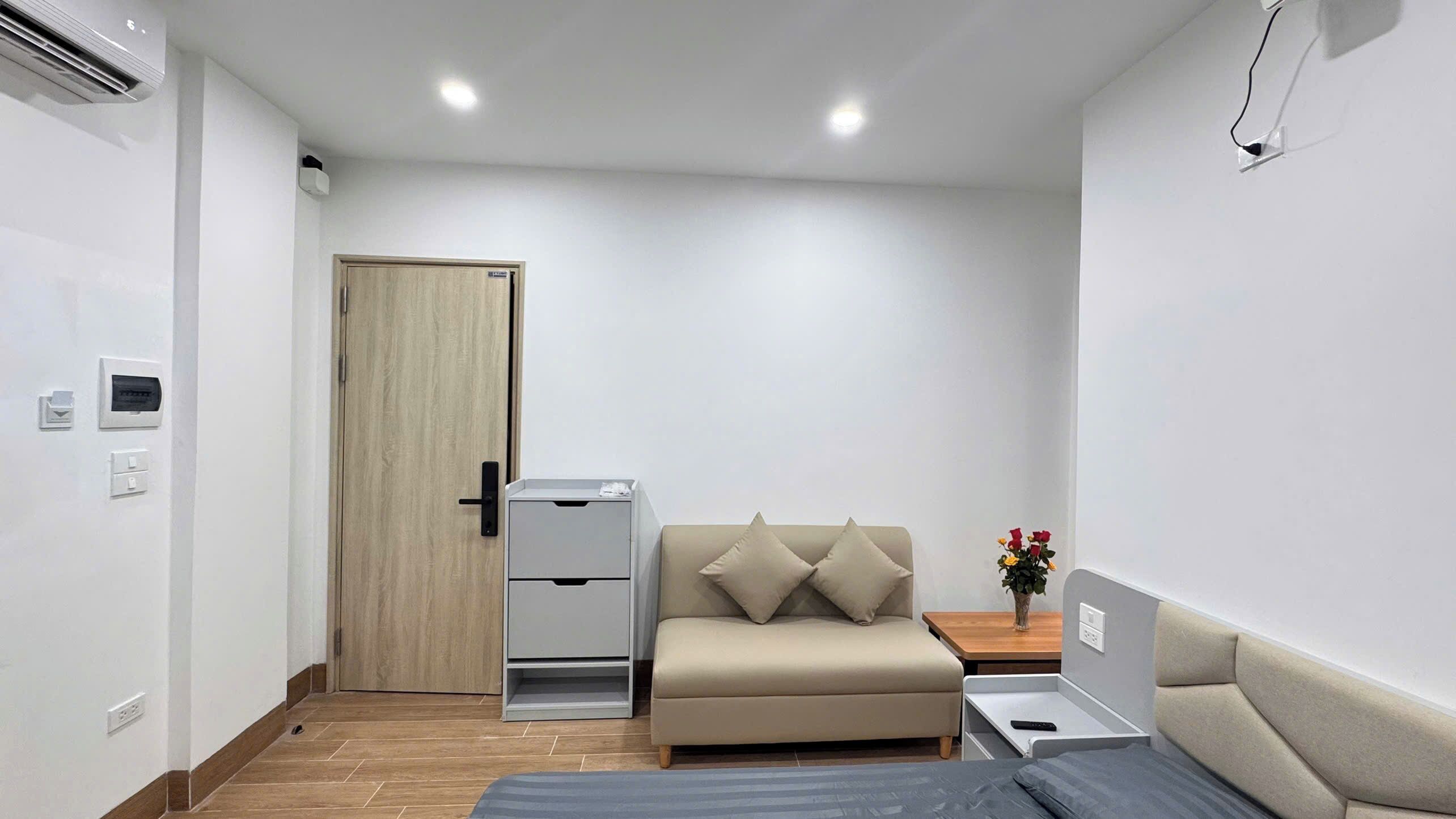 Ein kleiner, moderner Raum mit einer Couch, einem Nachttisch und einer Wand-Klimaanlage.