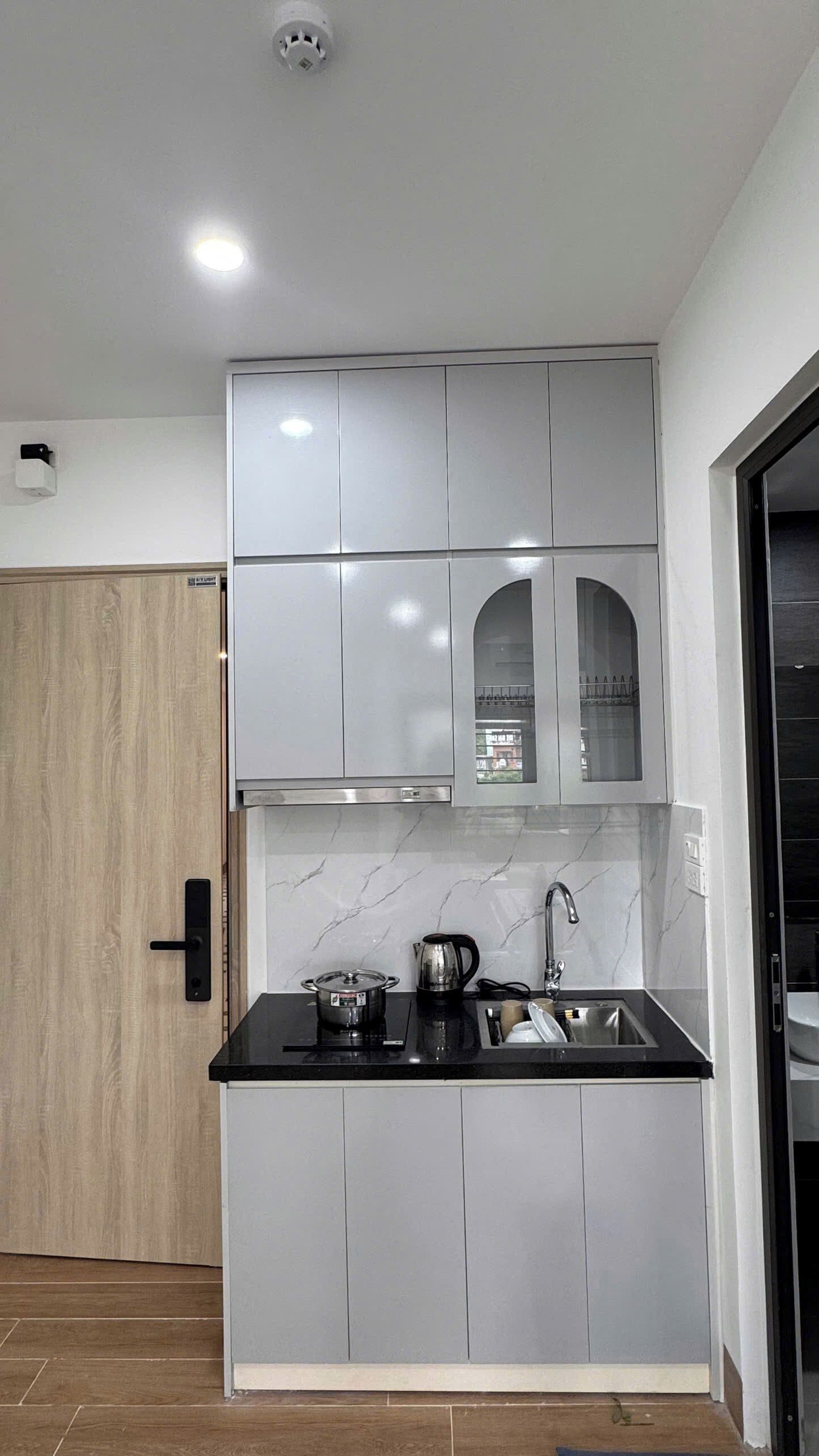 A modern kitchen with grey cabinets, a black countertop, and a stainless steel sink.