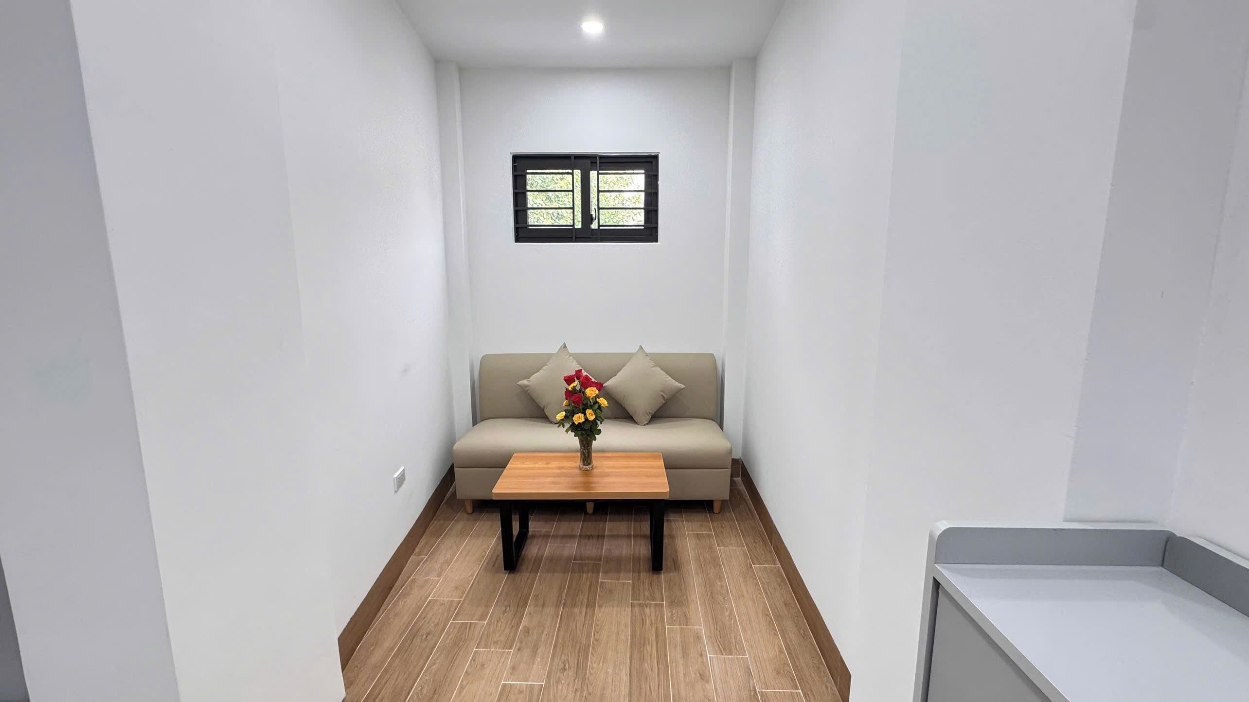 A narrow hallway with a sofa and a coffee table, a small window, and a tiled floor.