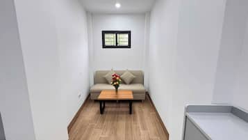 A narrow hallway with a sofa and a coffee table, a small window, and a tiled floor.