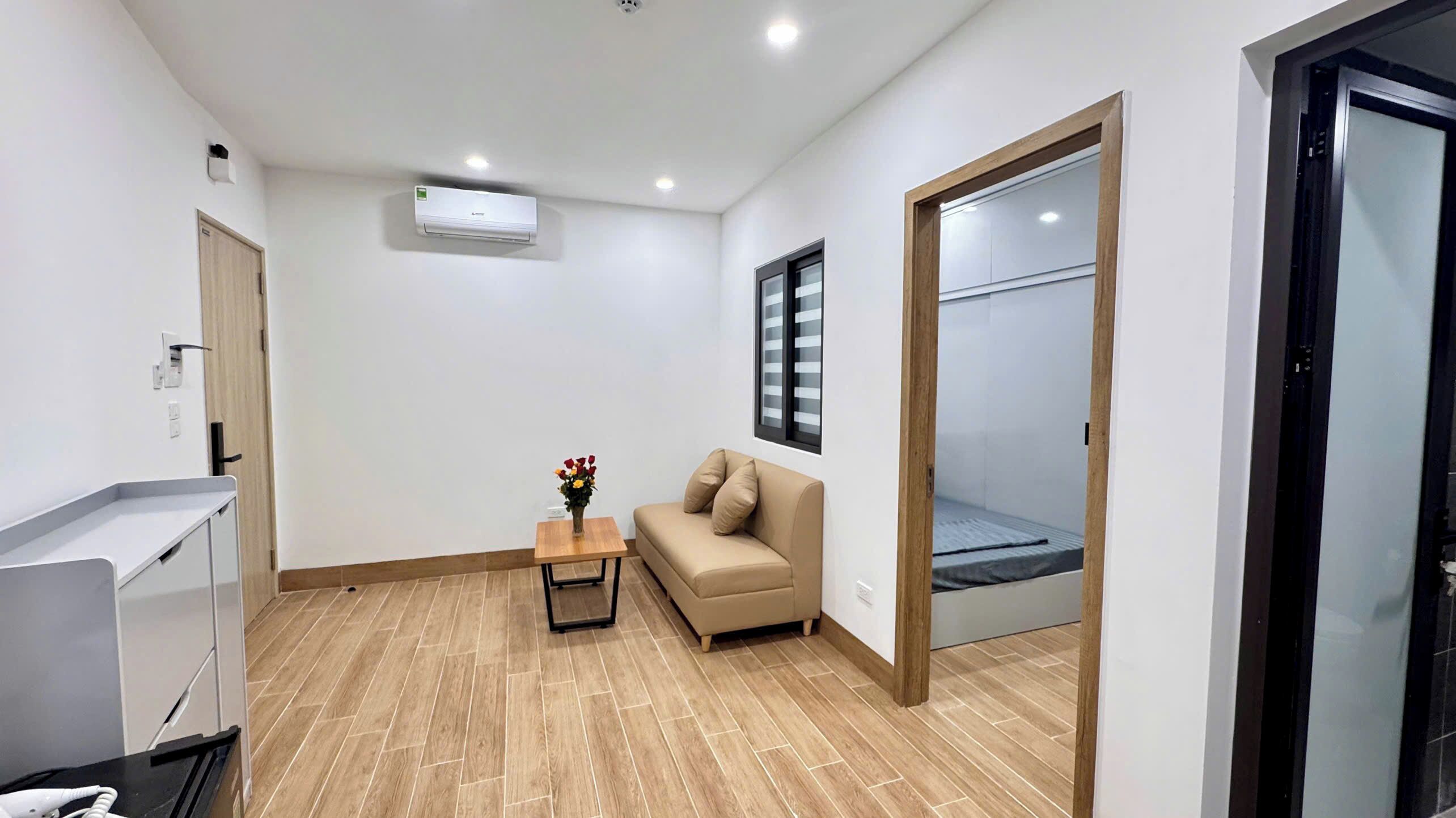 Ein Zimmer mit einer Couch, einem kleinen Tisch mit einer Vase, einem Fenster mit Jalousien und einer Klimaanlage.