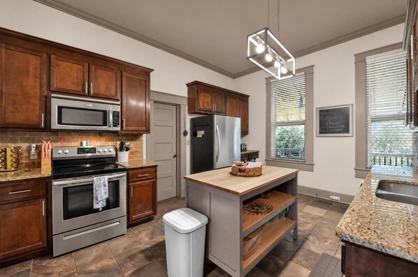 A modern kitchen with wooden cabinets, stainless steel appliances, and a granite countertop. - Crimson Rose Charmer | Walk to Bryant-Denny Stadium! (Tuscaloosa)