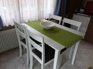 Ein Esstisch mit weißer Tischdecke und einer Schüssel darauf, umgeben von weißen Stühlen.