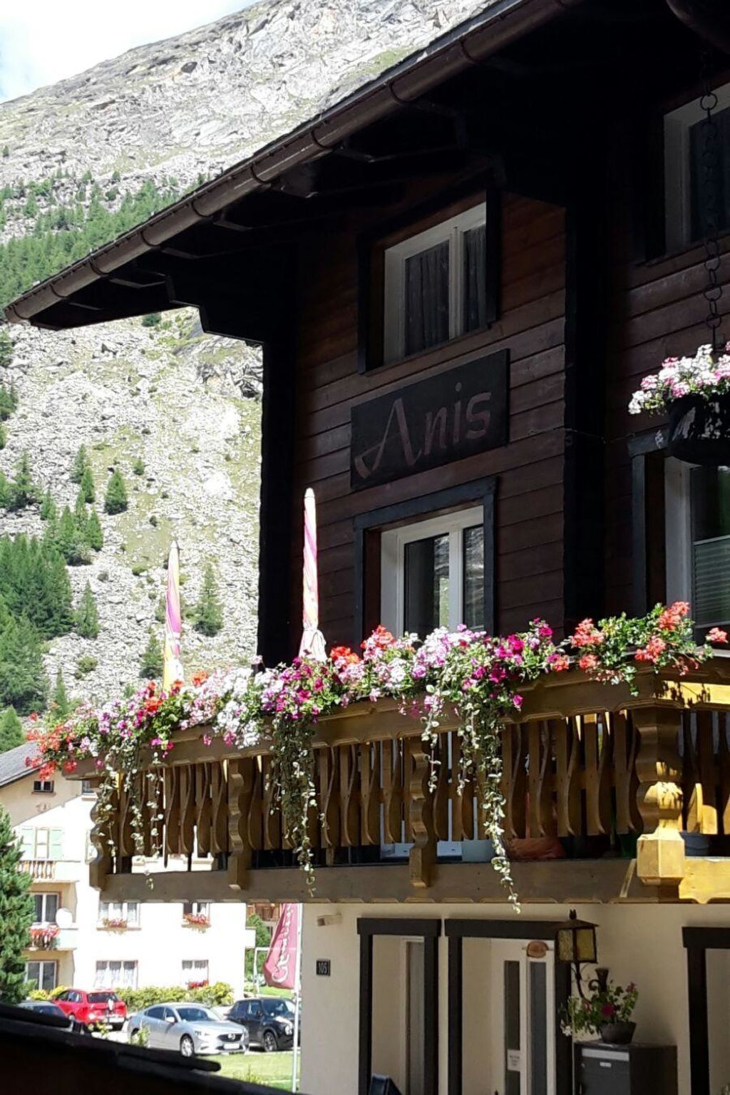 A wooden building with a balcony adorned with flowers and a sign that reads 'Anis.'
