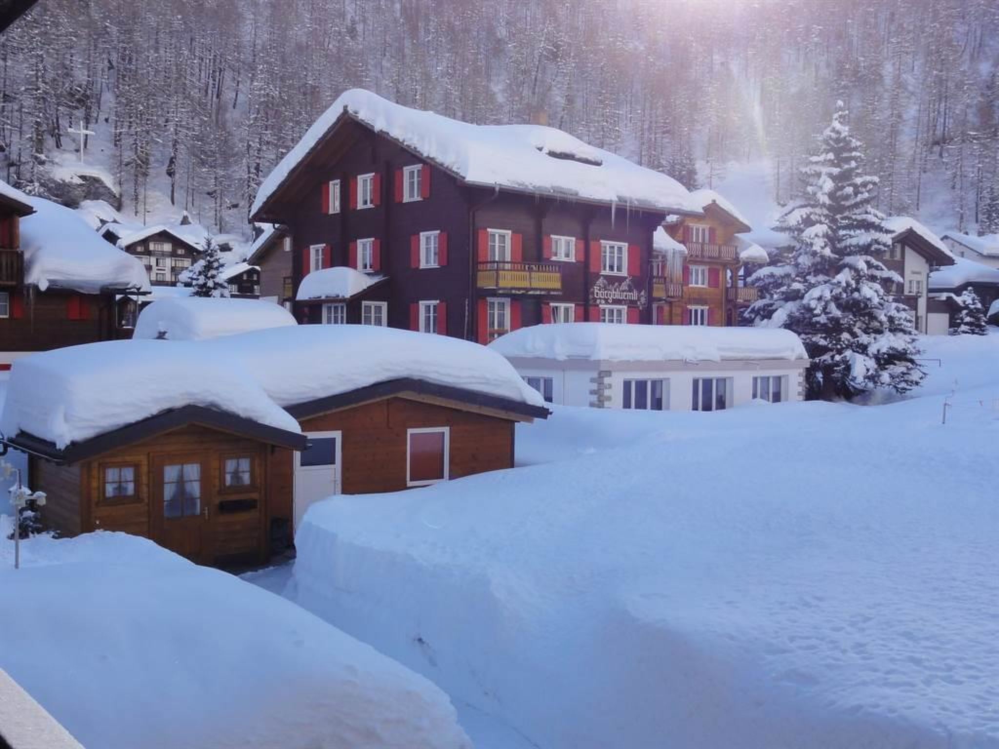 Un village enneigé, avec des bâtiments en bois et une chaîne de montagnes en arrière-plan.