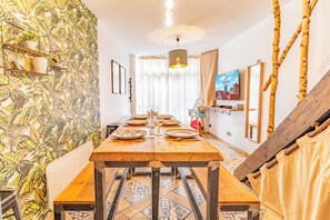 A dining area with a long wooden table set for a meal, surrounded by patterned wallpaper and a modern chandelier. - The red house Béthune - 2 minutes from the main square (Béthune)