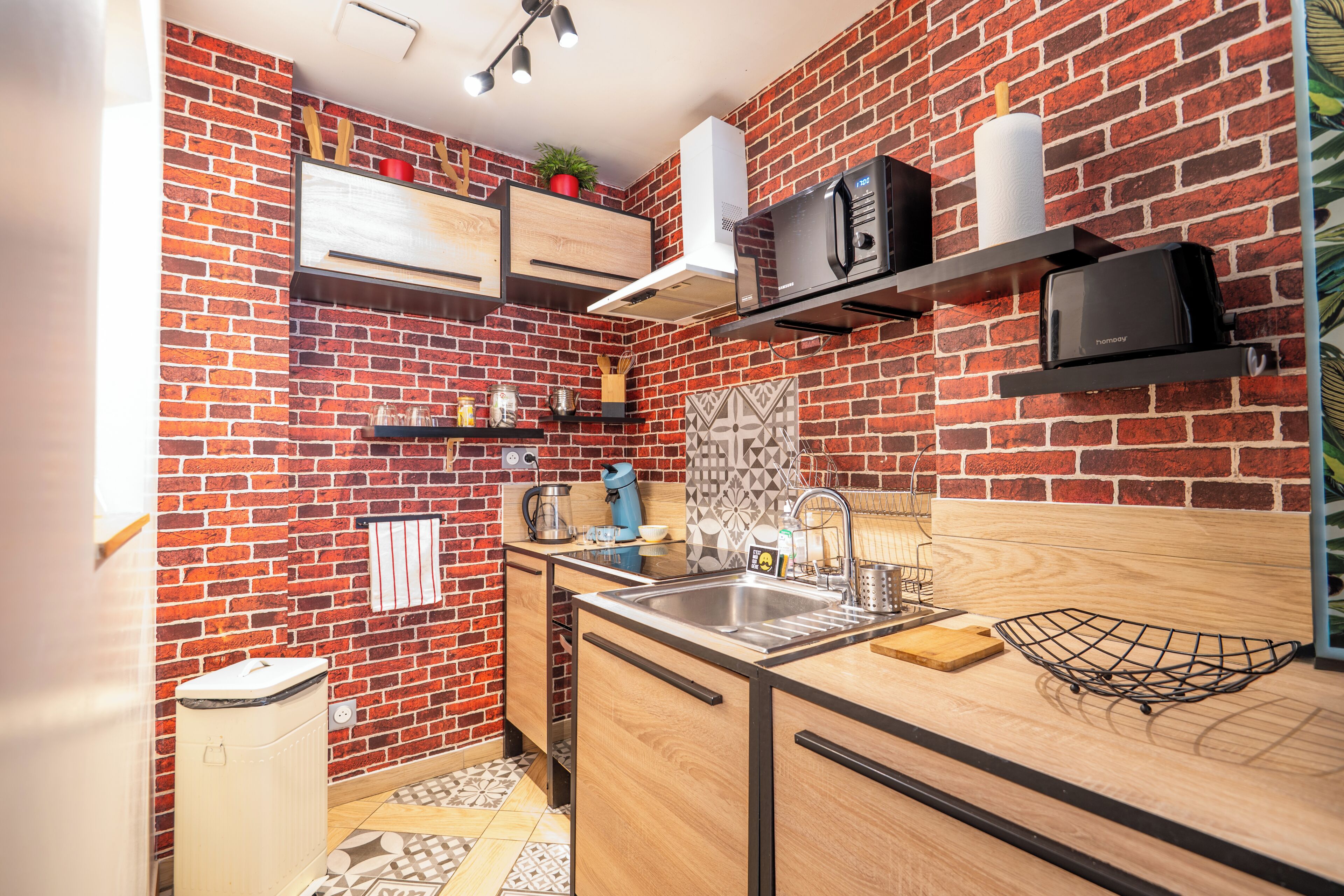 Una cocina compacta con pared de ladrillo, horno integrado, microondas y lavabo.
