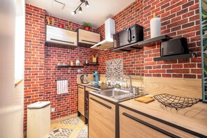 A compact kitchen with a brick wall, a built-in oven, a microwave, and a sink. - The red house Béthune - 2 minutes from the main square (Béthune)