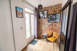 A room with a brick wall, a wooden floor, a yellow chair, and a door with a window. - The red house Béthune - 2 minutes from the main square (Béthune)