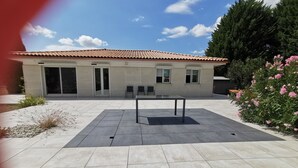 A patio with a table and chairs, a building with a tiled roof, and a garden with pink flowers. - House in the heart of the village (Chevanceaux)