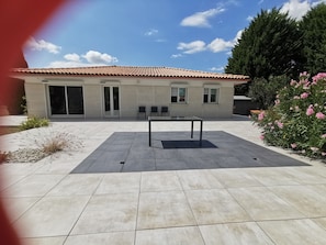 A patio with a table and chairs, a building with a tiled roof, and a garden with pink flowers. - House in the heart of the village (Chevanceaux)
