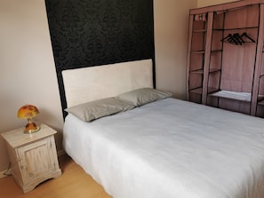 A bedroom with a bed, a nightstand with a lamp, a wardrobe, and a patterned wall. - House in the heart of the village (Chevanceaux)