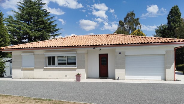 A single-story building with a red-tiled roof, a front door, and a garage door. - House in the heart of the village (Chevanceaux)