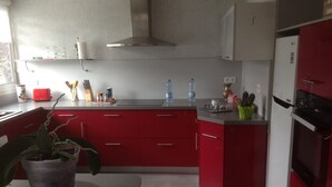 A modern kitchen with red cabinets, a stainless steel range hood, and a refrigerator. - House in the heart of the village (Chevanceaux)