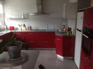 A modern kitchen with red cabinets, a stainless steel range hood, and a refrigerator. - House in the heart of the village (Chevanceaux)