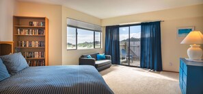 A bedroom with a large bed, a bookshelf, a window with curtains, and a view of the outdoors. - Mare Vista (TOT # 2194): 2  BR, 2  BA House in The Sea Ranch, Sleeps 4 (The Sea Ranch)