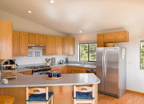 A modern kitchen with wooden cabinets, a stainless steel refrigerator, and a large island with bar stools. - Mare Vista (TOT # 2194): 2  BR, 2  BA House in The Sea Ranch, Sleeps 4 (The Sea Ranch)