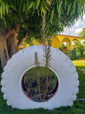 A tire planter with plants, a tree, and a yellow building in the background. - 4-Min Walk to Bio Bay & Beach • Beach Day Ready (Esperanza)