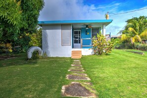 A small house with a blue roof and white walls, a front door, and a small porch with a chair.