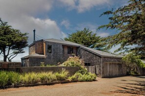 A two-story stone building with a sloped roof, surrounded by vegetation and a clear sky. - Autumn Mist TOT #2141: 2  BR, 2.5  BA House in The Sea Ranch, Sleeps 4 (The Sea Ranch)