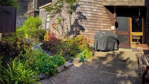 A covered outdoor seating area with a grill, surrounded by a garden with various plants and shrubs. - Autumn Mist TOT #2141: 2  BR, 2.5  BA House in The Sea Ranch, Sleeps 4 (The Sea Ranch)